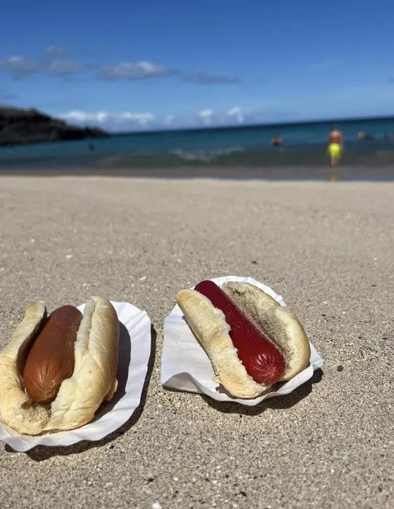 Two Uncle Al's hot dogs with ketchup in paper boats on the sand at the beach