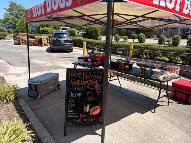 An outdoor Hot Dogs tent with a chalkboard reading Happy National Hot Dog Day and a toppings bar