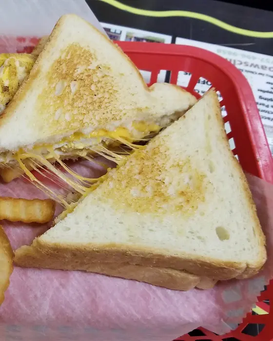 A grilled cheese sandwich pulled apart with melted cheese, crinkle fries beside it in a red basket